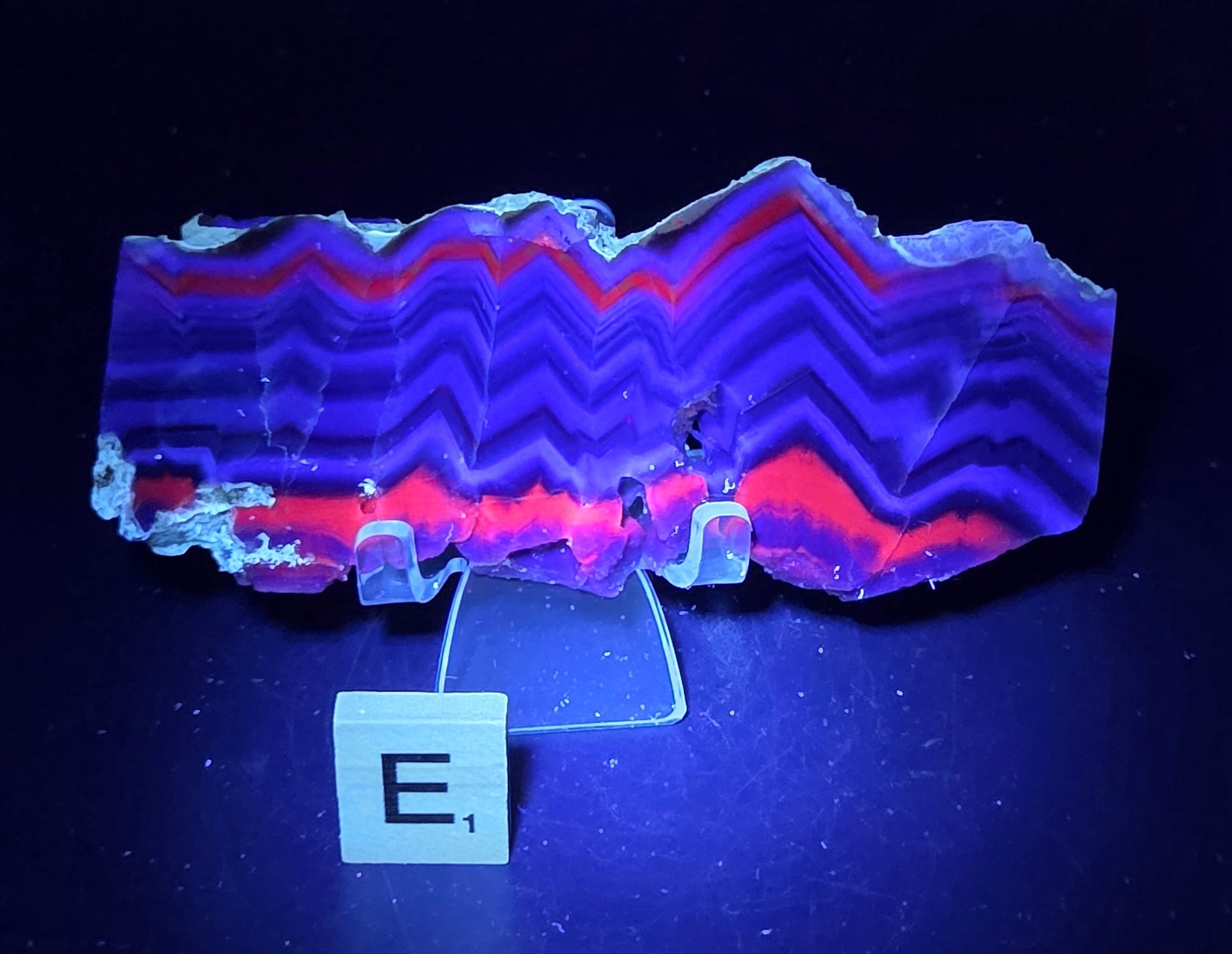 Banded fluorite slab under UV light on a stand against a neutral background
