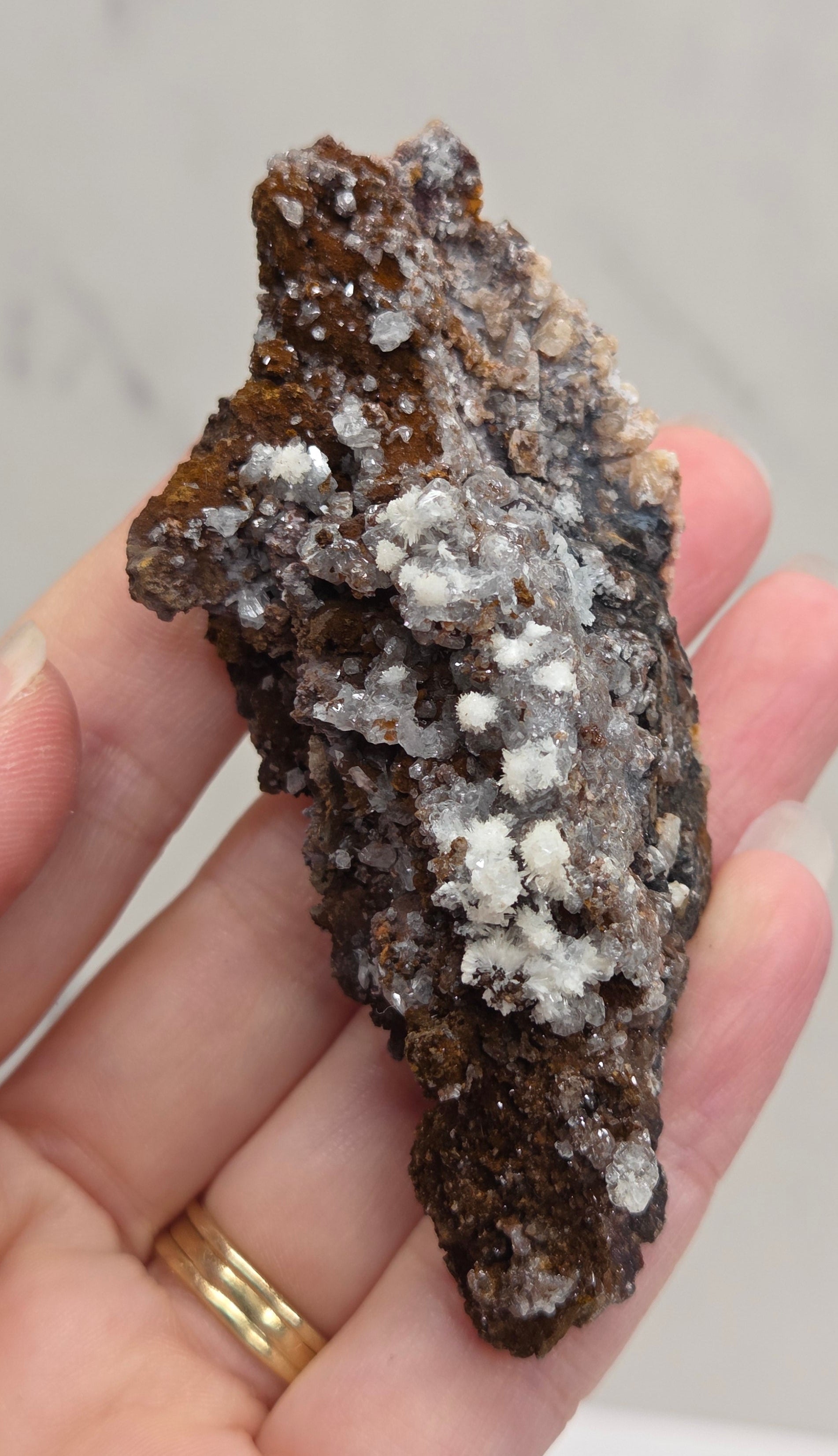 Hand holding a rock with white crystals against a neutral background