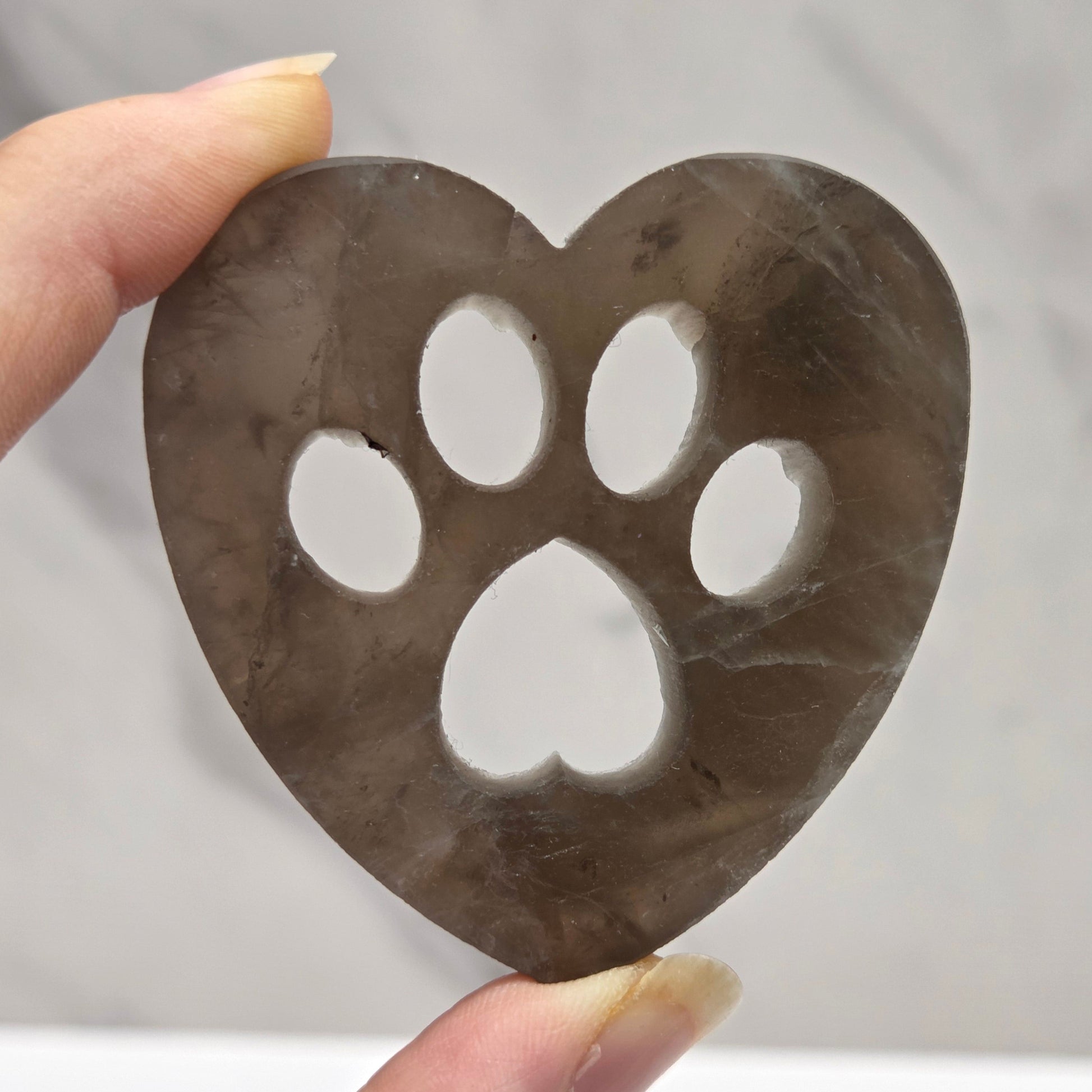 Fingers holding a heart carving with a paw print on a white background