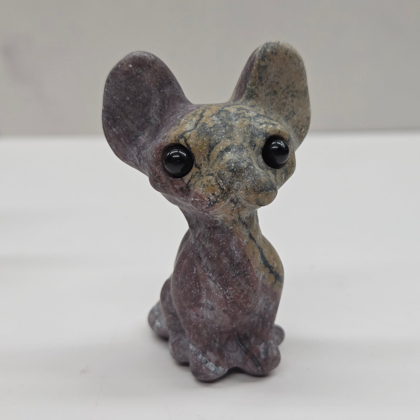 Small gray figurine of a cat with large eyes on a white surface