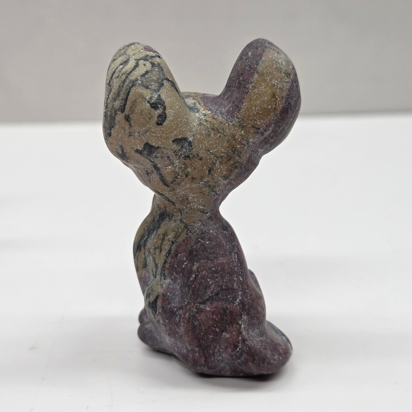 Small stone sculpture of a cat on a white surface with a gray background