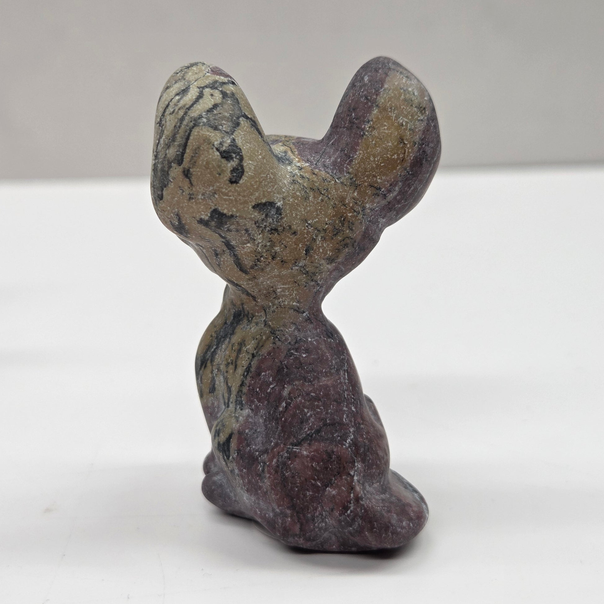 Small stone sculpture of a cat on a white surface with a gray background