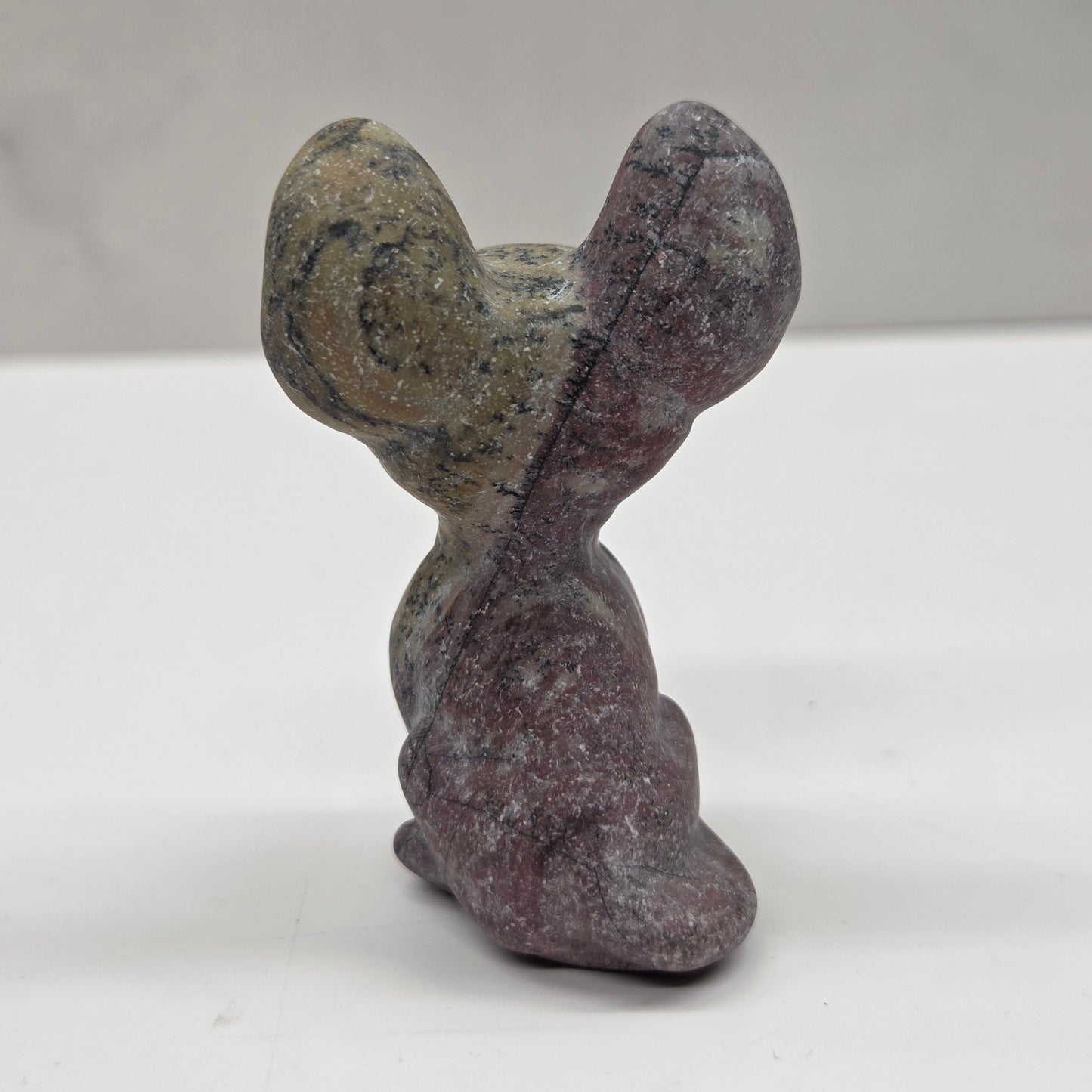 Small gray figurine of a cat with large eyes on a white surface