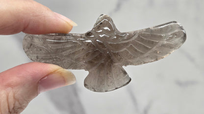 Hand holding a Smoky Quartz eagle carving on a white background