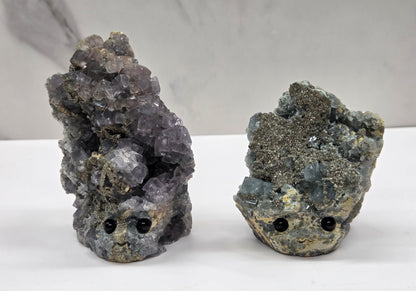 Two fluorite figurines with black eyes on a white surface and marble background