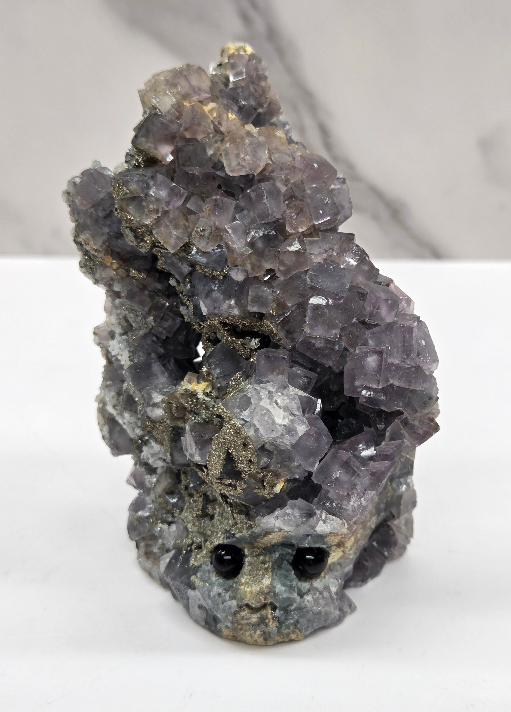 fluorite figurine with black eyes on a white surface and marble background