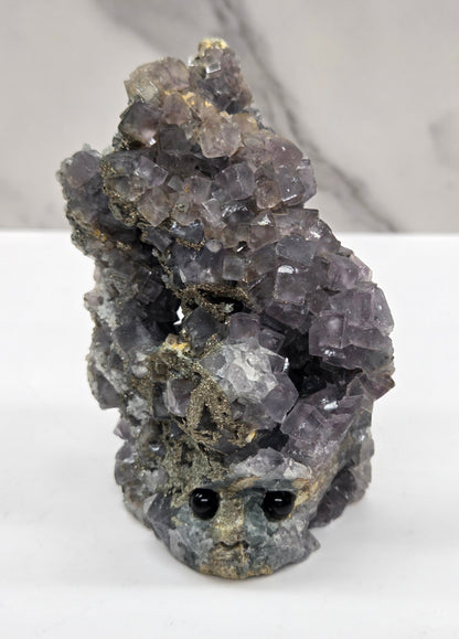 fluorite figurine with black eyes on a white surface and marble background