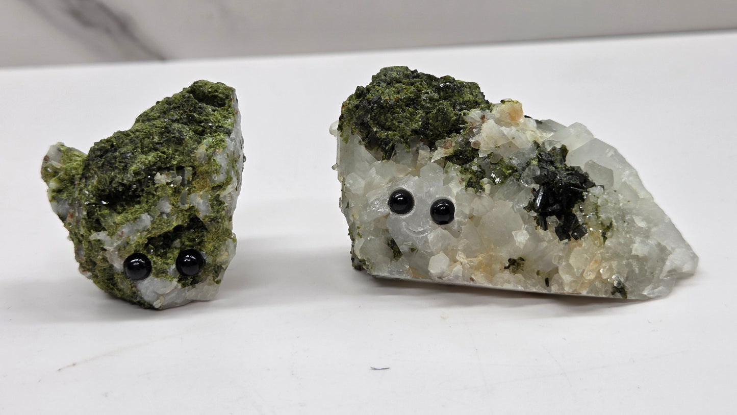 Epidote on quartz carved into a groot like carving with eyes and a mouth on a white background