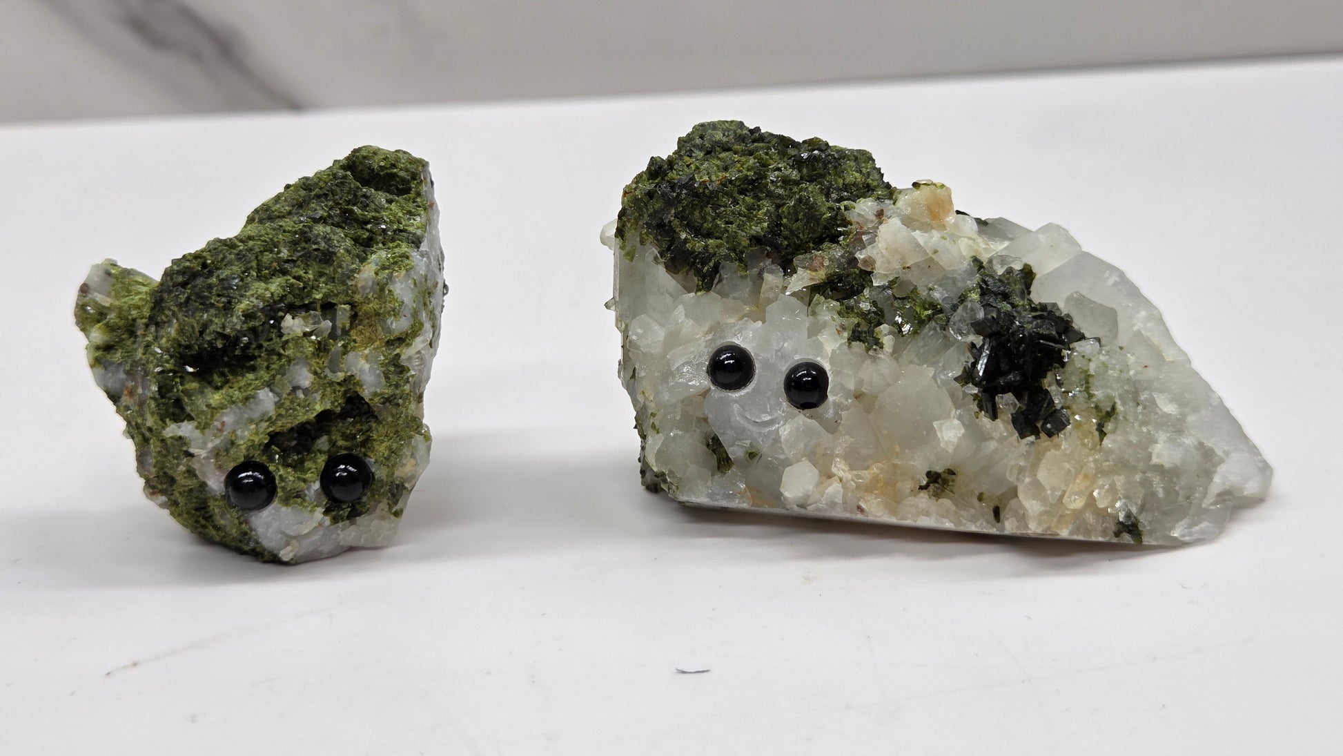 Epidote on quartz carved into a groot like carving with eyes and a mouth on a white background