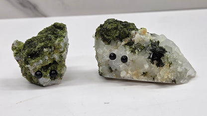 Epidote on quartz carved into a groot like carving with eyes and a mouth on a white background