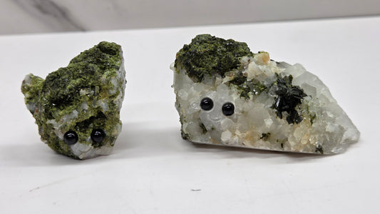 Epidote on quartz carved into a groot like carving with eyes and a mouth on a white background