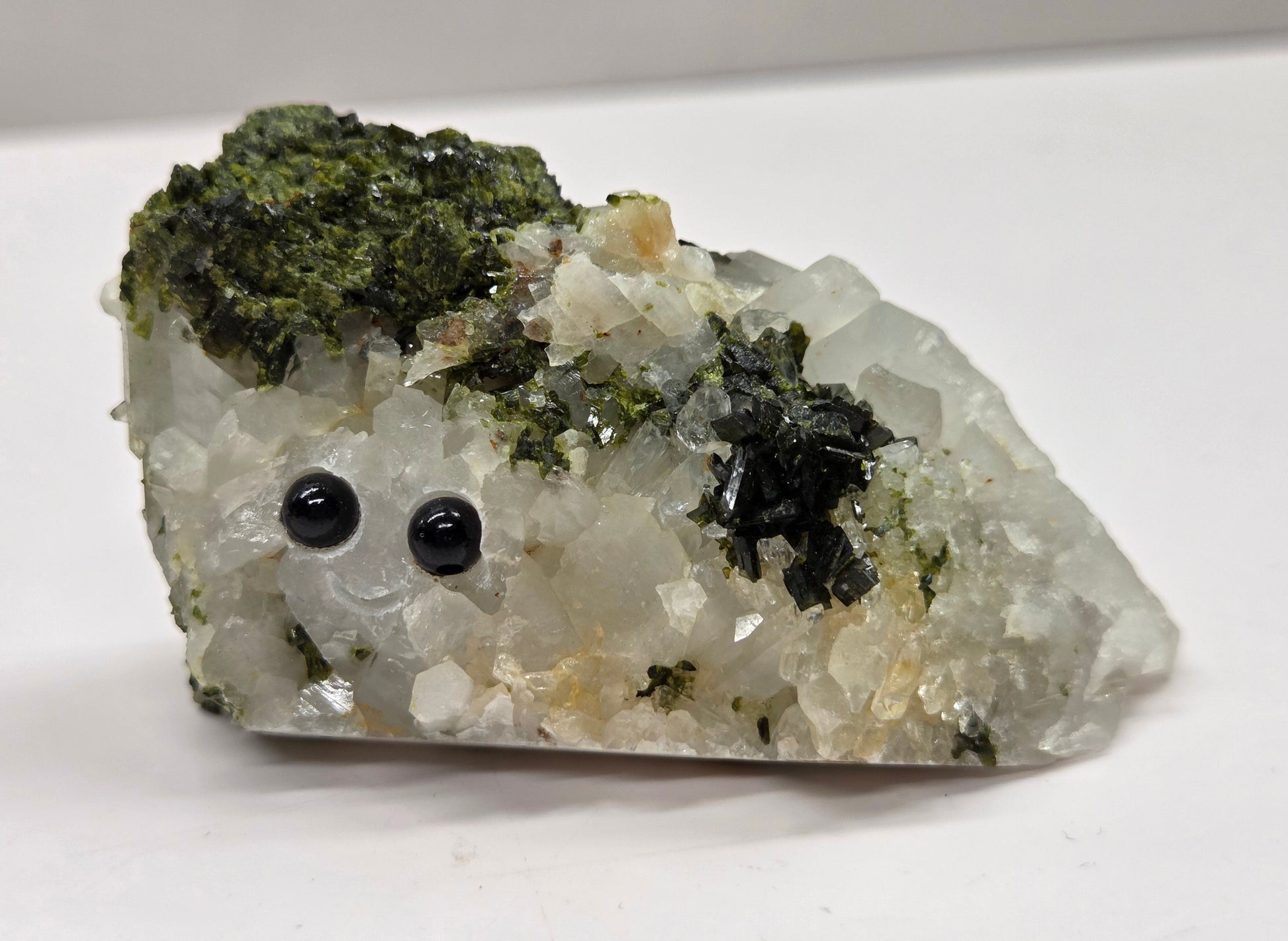 Epidote on quartz carved into a groot like carving with eyes and a mouth on a white background