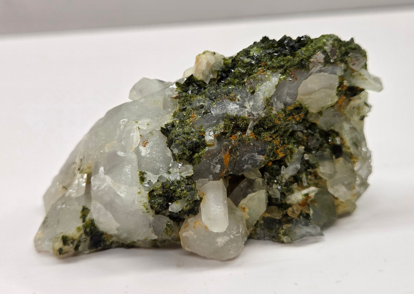 Epidote on quartz carved into a groot like carving with eyes and a mouth on a white background