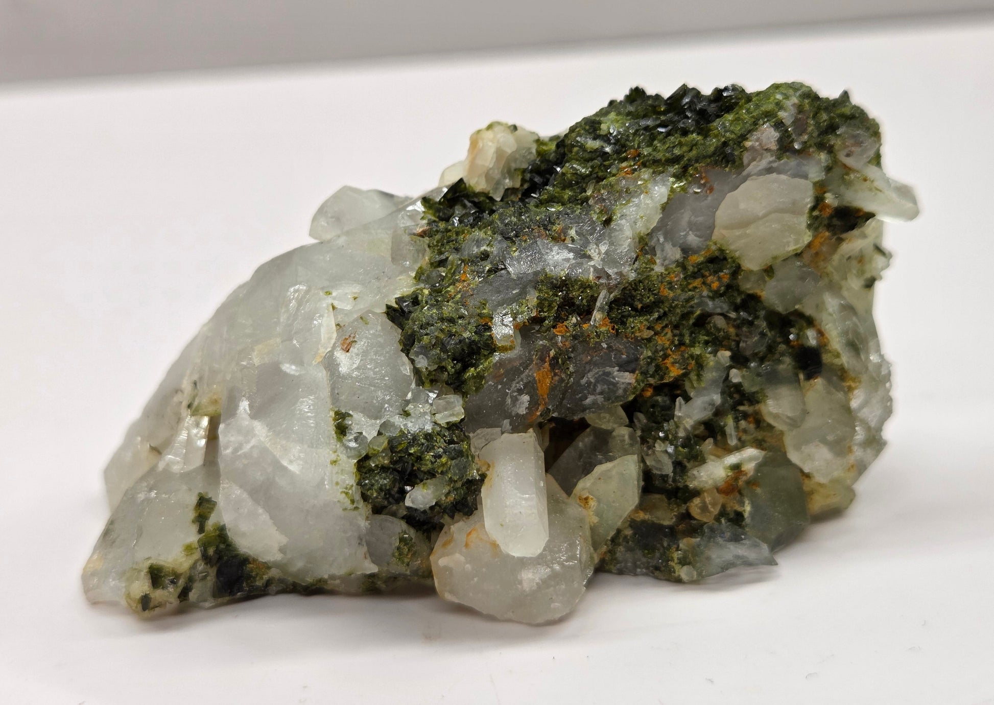 Epidote on quartz carved into a groot like carving with eyes and a mouth on a white background