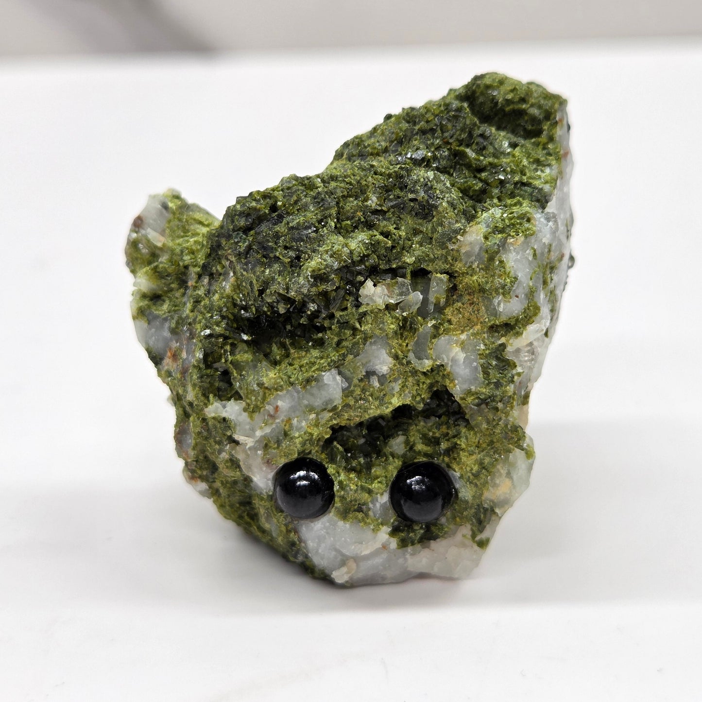 Epidote on quartz carved into a groot like carving with eyes and a mouth on a white background