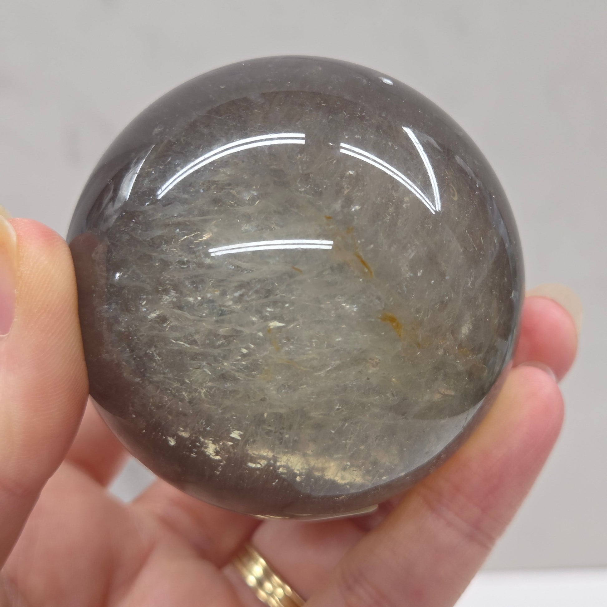 Hand holding a dark gray crystal ball against a neutral background