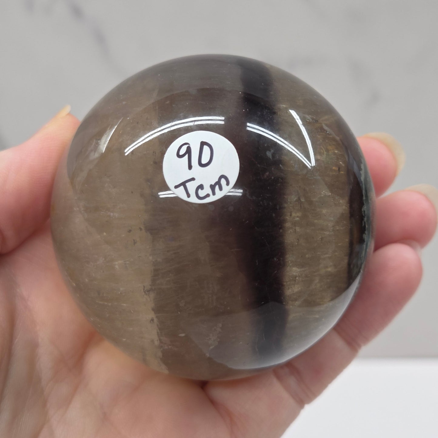 Hand holding a clear crystal ball with a logo and text on a neutral background