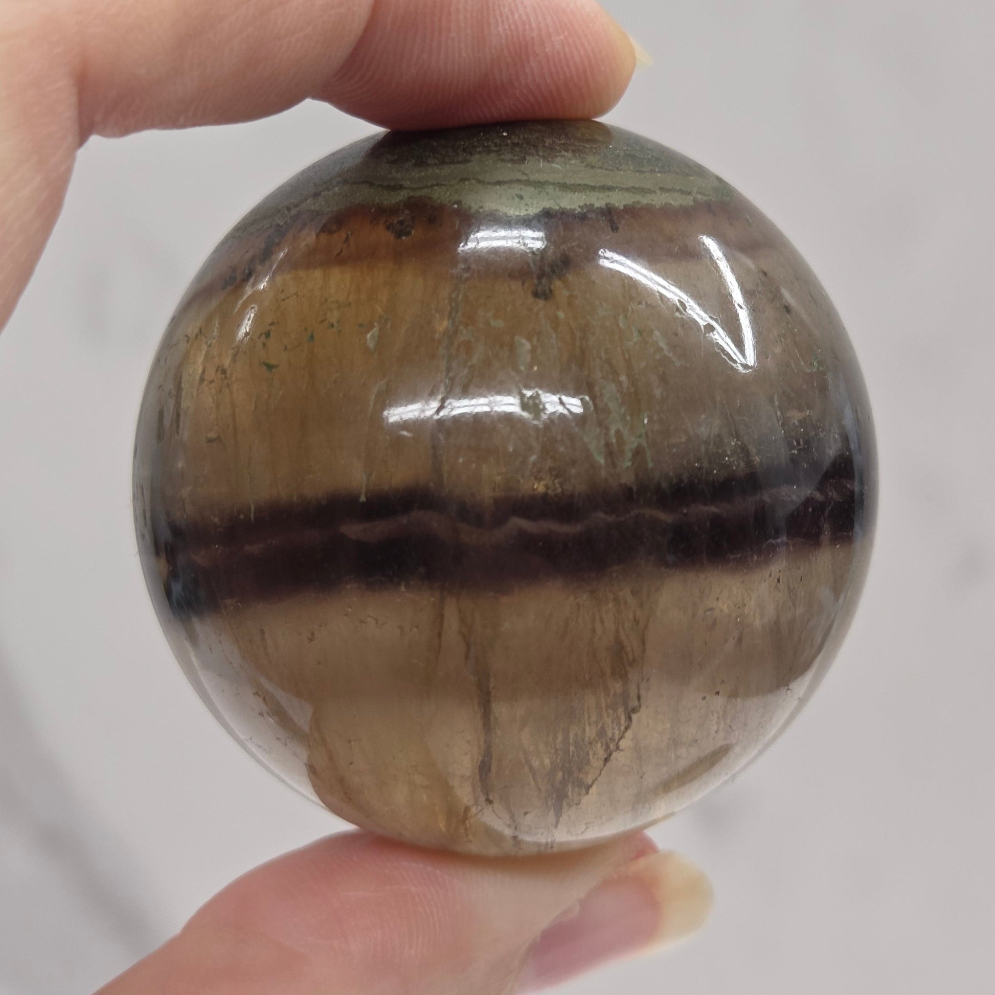 Hand holding a striped crystal ball against a neutral background