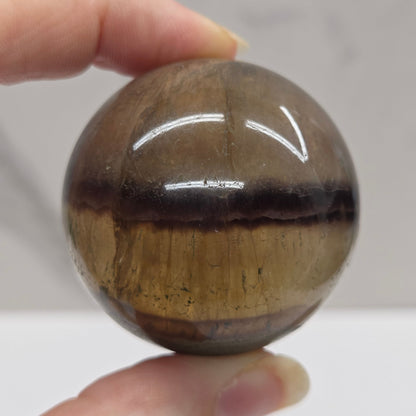Hand holding a brown crystal ball against a neutral background