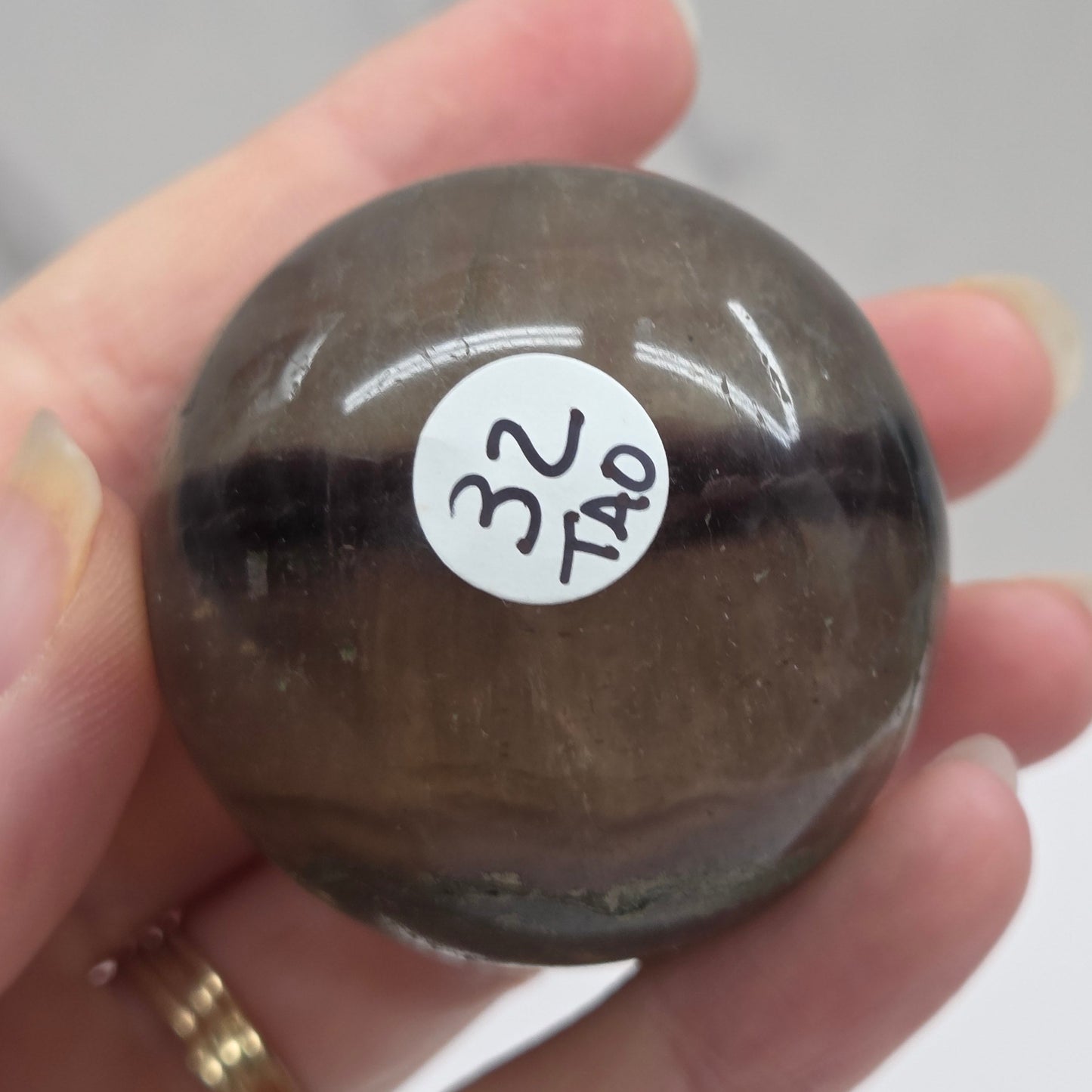 Hand holding a dark brown stone with a label on a neutral background