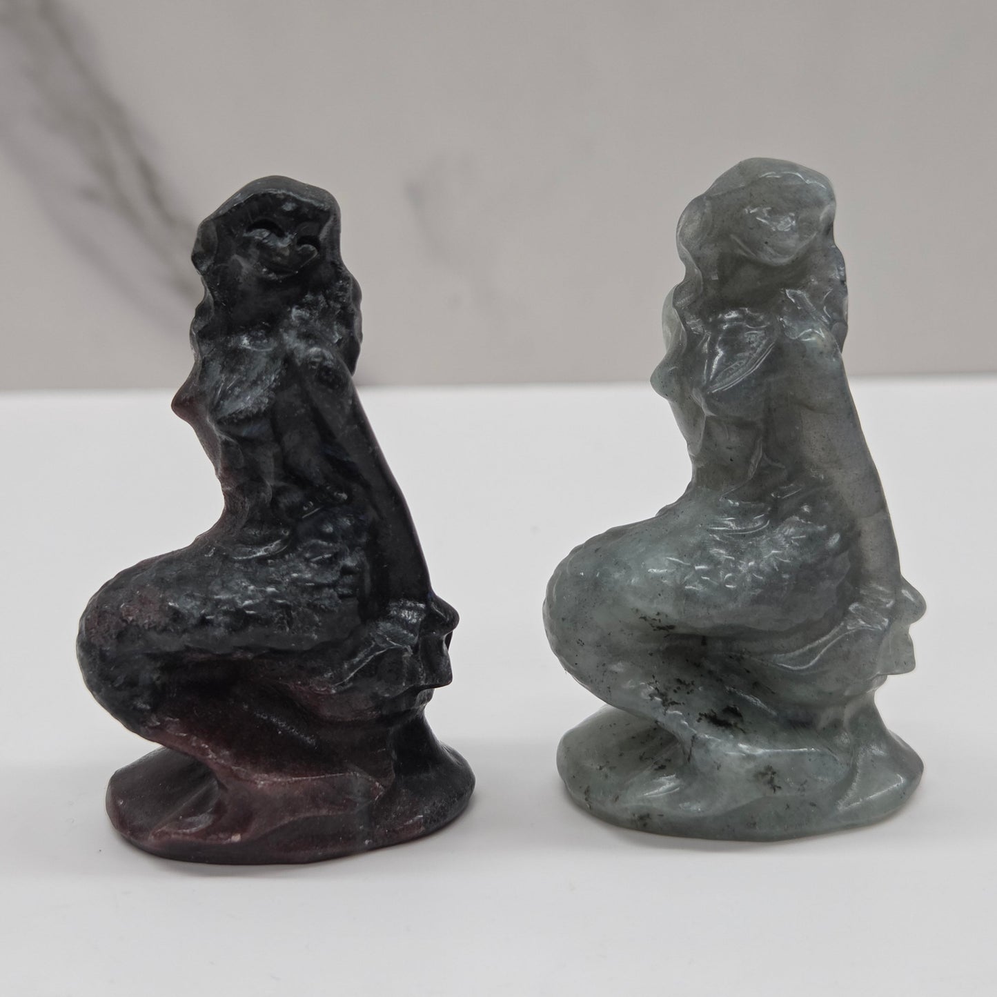 Two stone sculptures of women on a white surface with a gray background