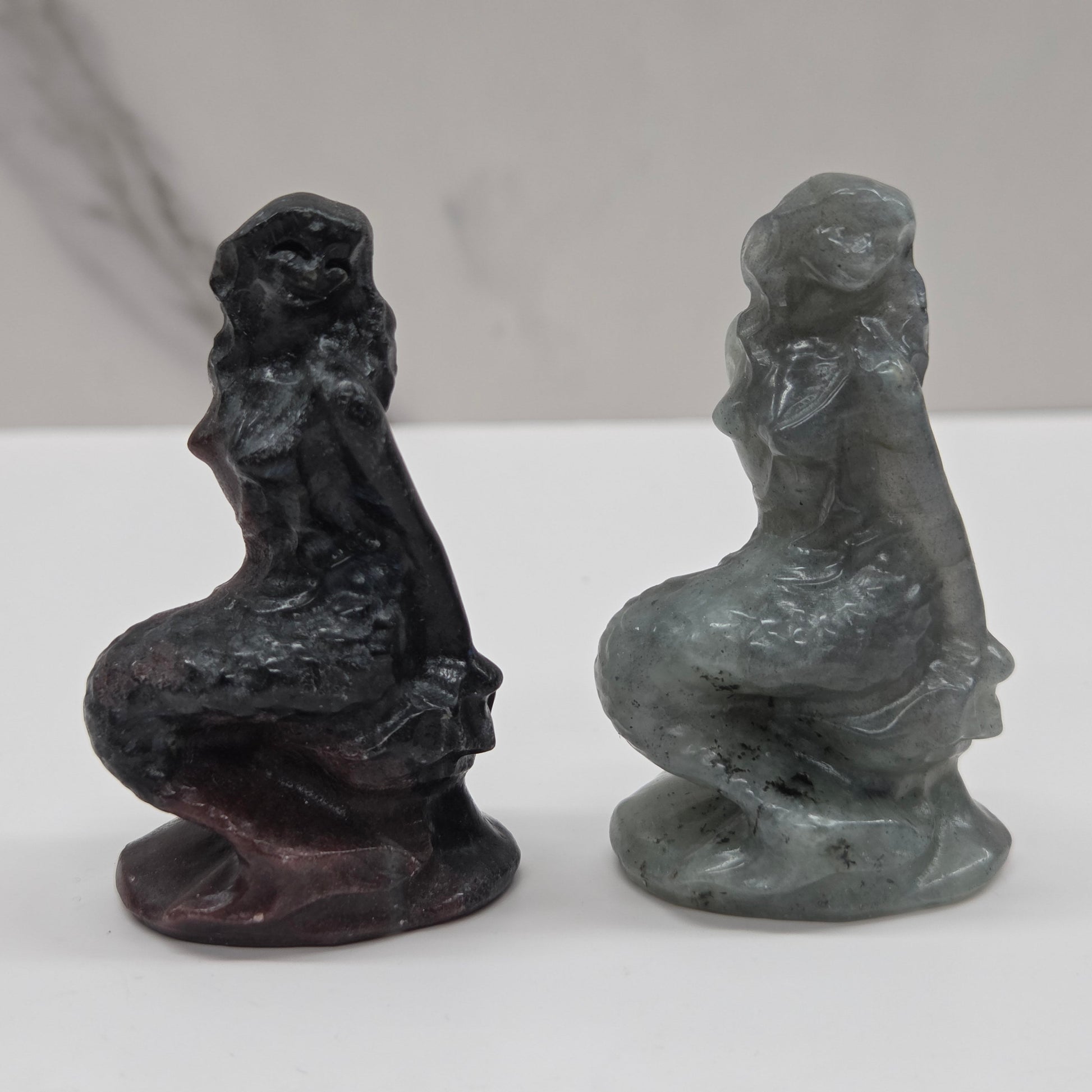 Two stone sculptures of women on a white surface with a gray background