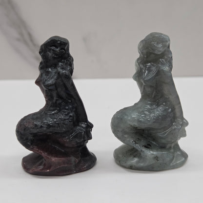 Two stone sculptures of women on a white surface with a gray background
