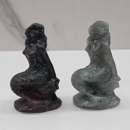 Two stone sculptures of women on a white surface with a gray background