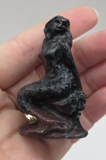Hand holding a mermaid carving against a plain background