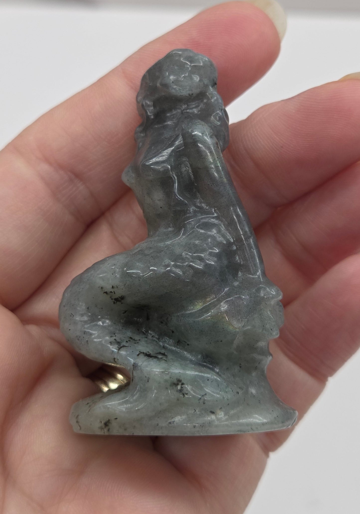 Small gray mermaid figurine held in a hand against a neutral background