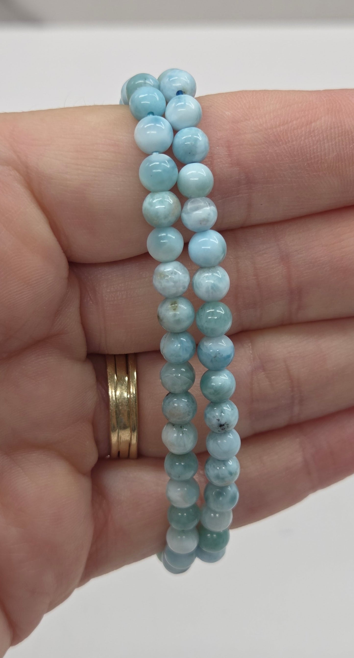 Two light blue beaded bracelets on a hand with a plain background