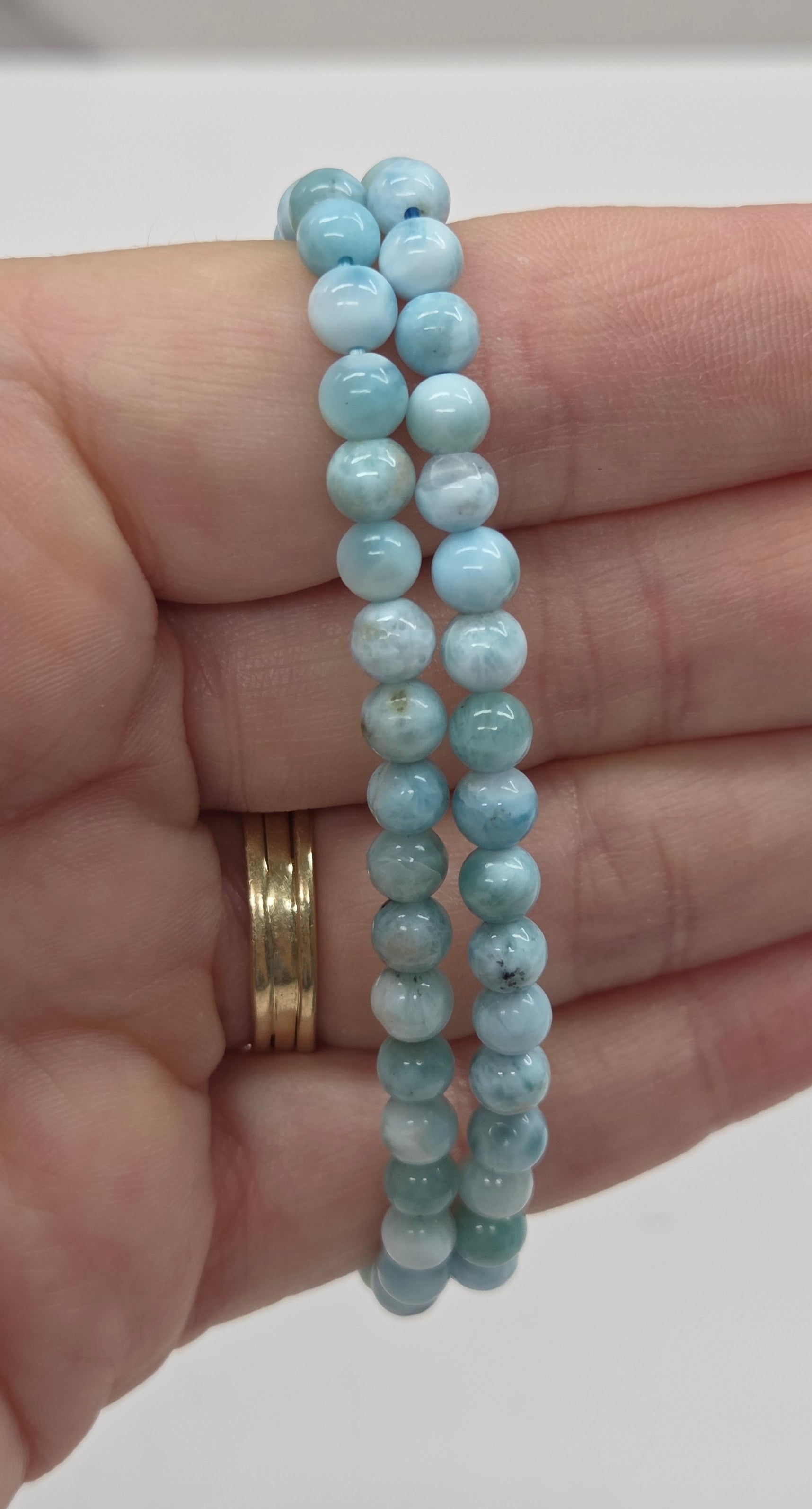 Two light blue beaded bracelets on a hand with a plain background