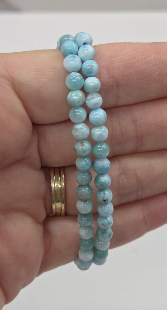 Two light blue beaded bracelets on a hand with a plain background