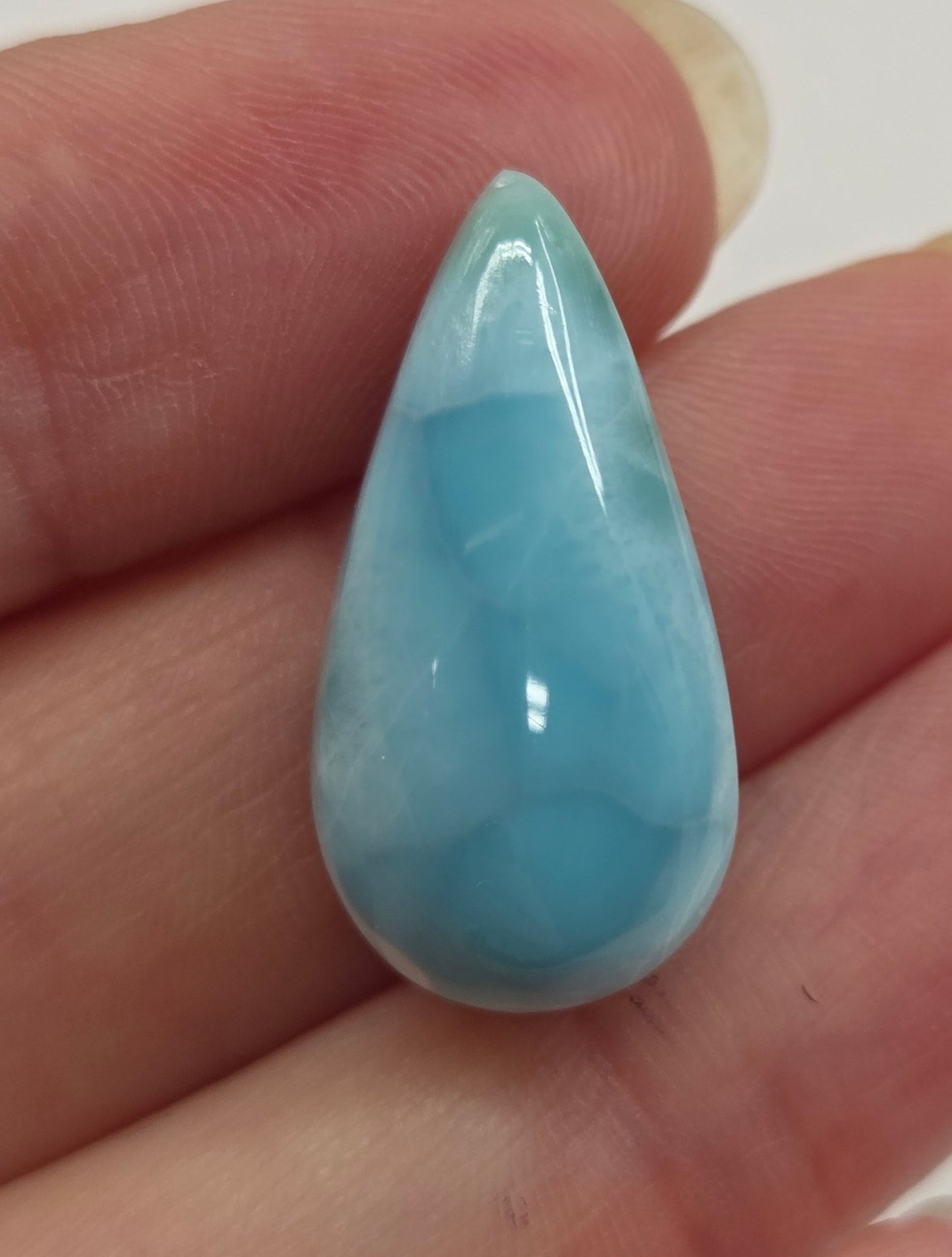 Hand holding a blue larimar stone against a white background