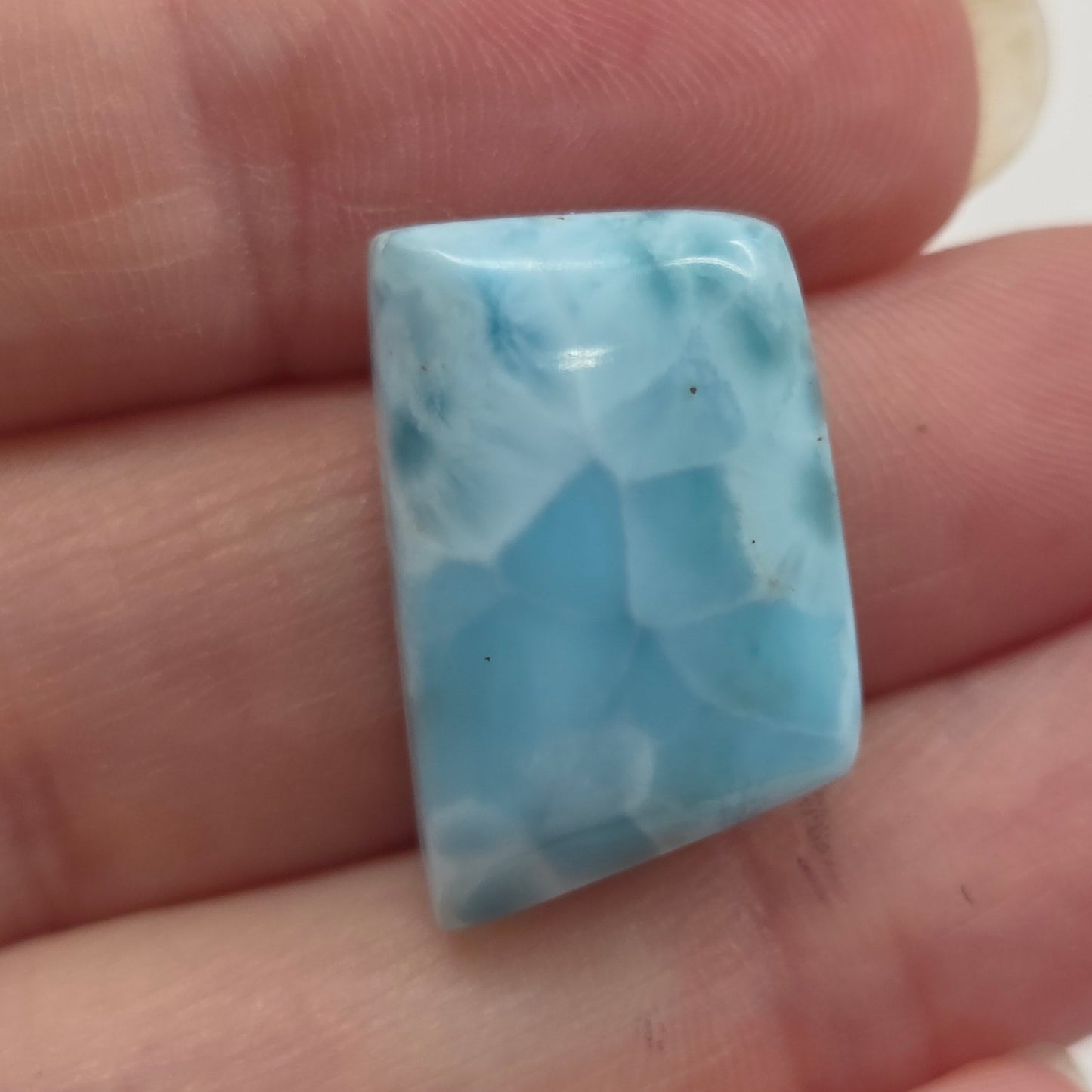 Blue marbled stone on a person's finger against a white background