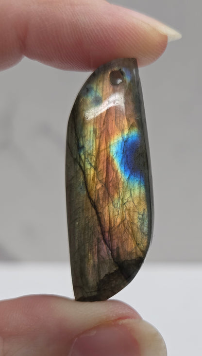 Multicolored labradorite stone held between fingers against a neutral background