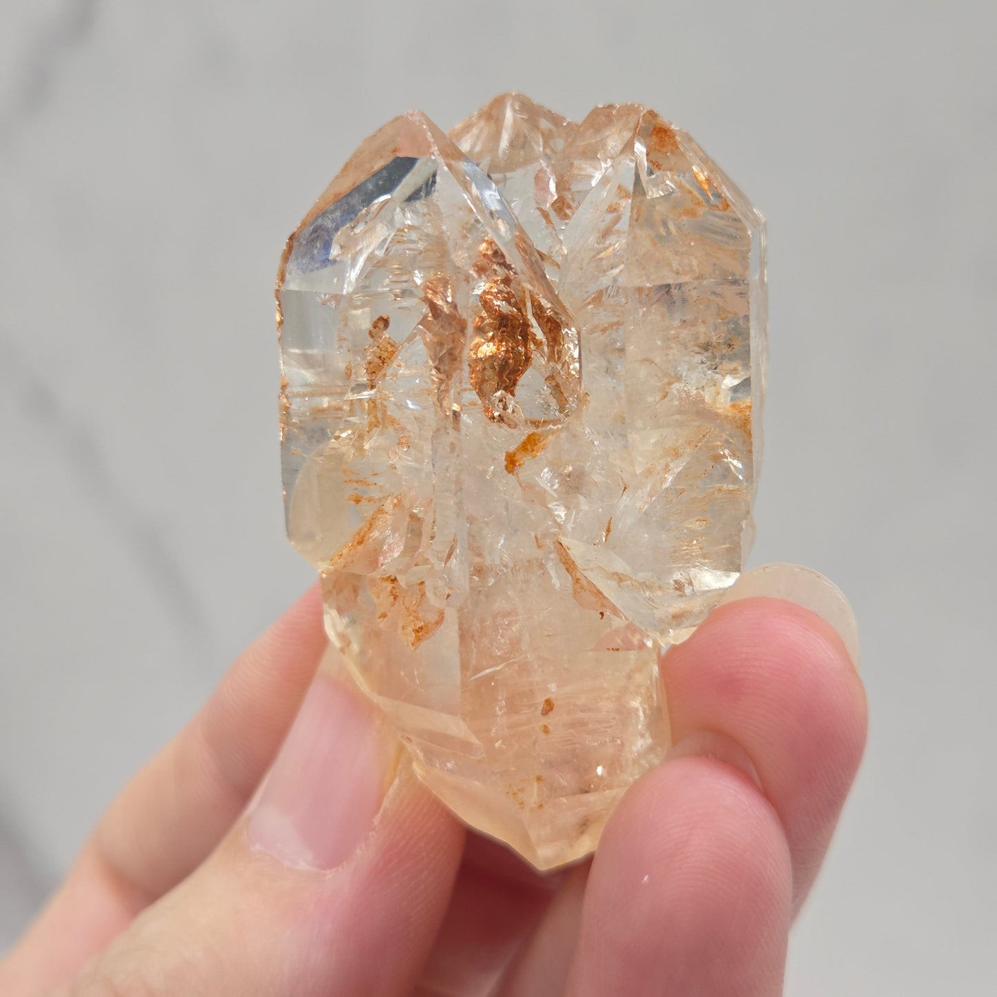 Hand holding a clear crystal with gold inclusions against a neutral background