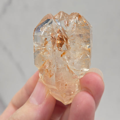 Hand holding a clear crystal with gold inclusions against a neutral background