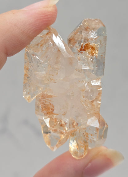Clear crystal rock held by a hand against a neutral background