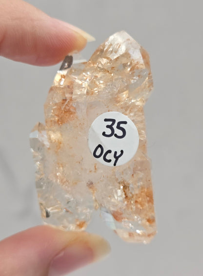 Clear crystal rock held by a hand against a neutral background