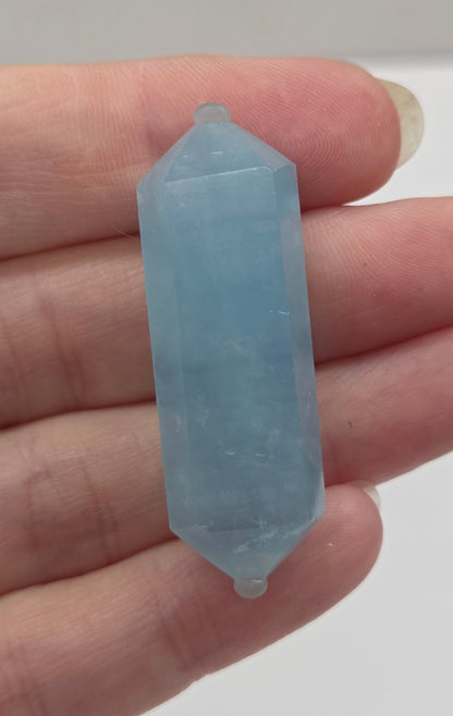 Hand holding a light blue crystal against a white background