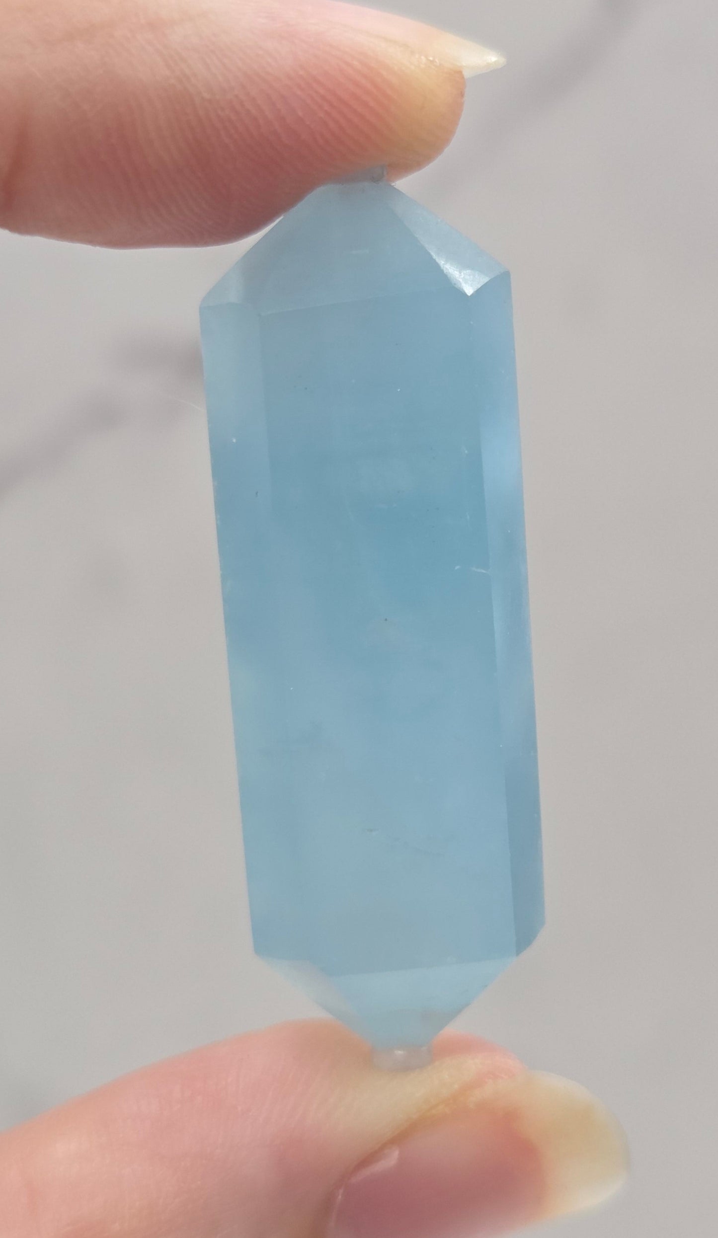 Hand holding a light blue crystal against a neutral background