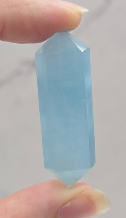 Hand holding a light blue crystal against a neutral background