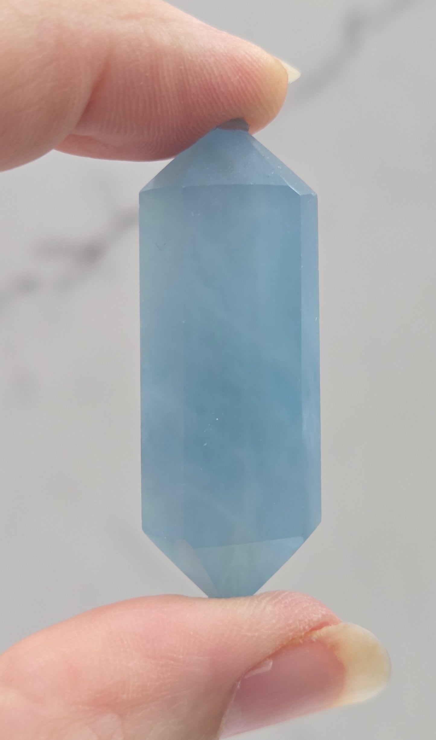 Hand holding a blue crystal against a neutral background