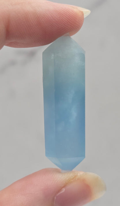 Hand holding a light blue crystal against a neutral background