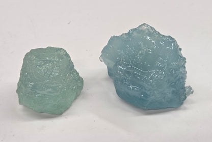 Two rough blue-green crystals on a white background