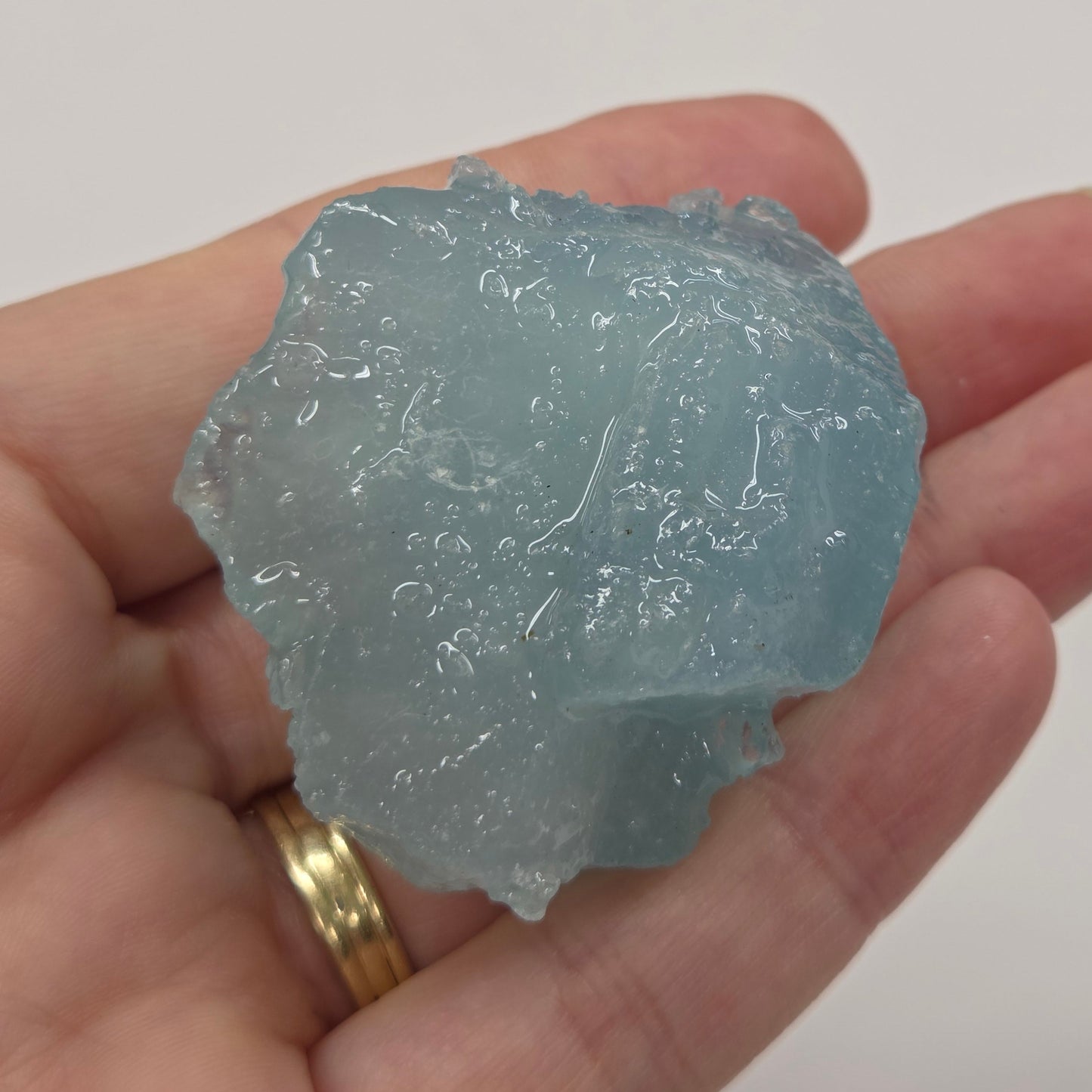 Hand holding a rough crystal against a plain background
