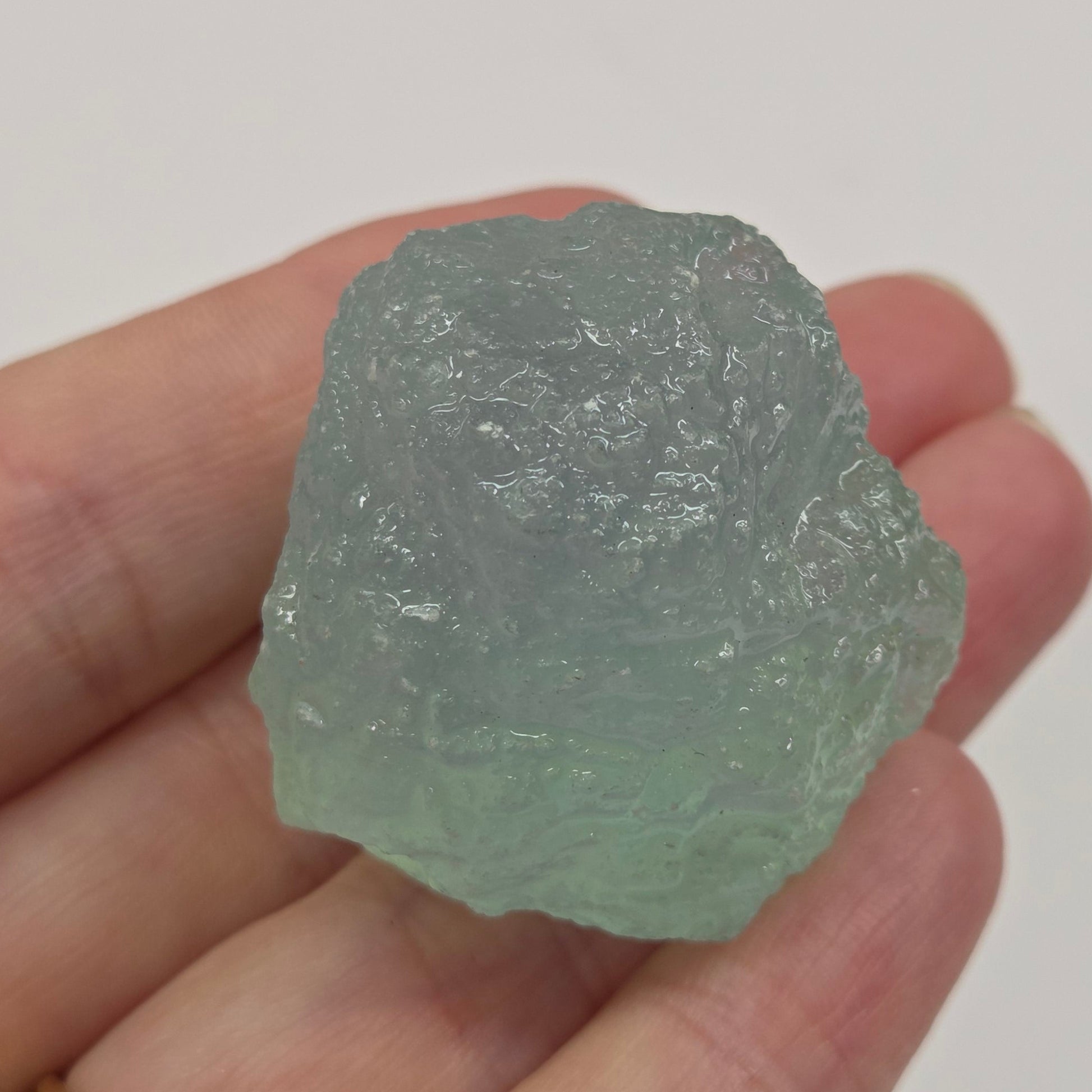 Hand holding a rough crystal rock against a plain background