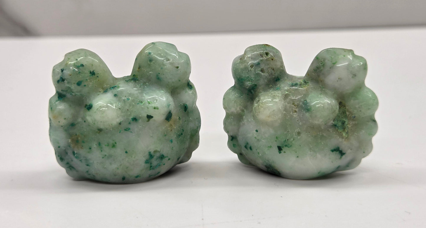 Two green stone carvings resembling crabs on a white surface.
