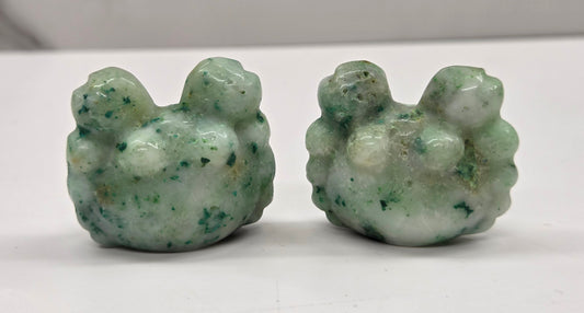 Two green stone carvings resembling crabs on a white surface.
